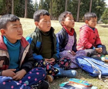 stress | Hemophilia News Today | Four children meditate at the Jhamtse Gatsal Children's Community in India. The boys are seated on the ground outside with their legs crossed and their eyes closed.