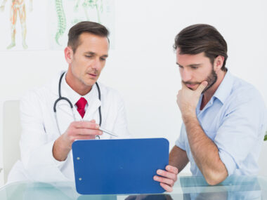 A male patient speaking with a doctor and looking at a chart.
