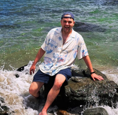 A man sits on a rock along a shoreline.