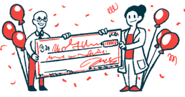 Two scientists each hold one end of a giant check amid balloons and confetti.