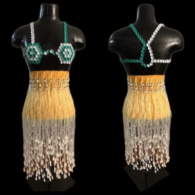 A top and skirt made from medical waste are shown on a mannequin against a black background. The skirt is made from butterfly needles, with orange butterfly wings at the top and tubing cascading down. Caps from saline syringes trim the skirt's waist. The top is made from the caps of factor VIII vials.